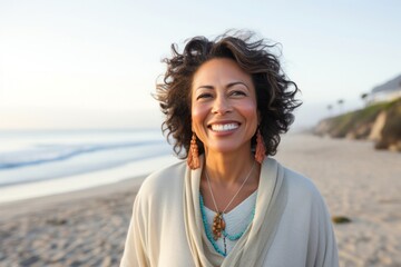 portrait of a happy Mexican woman in her 50s wearing a chic cardigan against a beach background