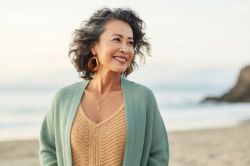 portrait of a Filipino woman in her 50s wearing a chic cardigan against a beach background