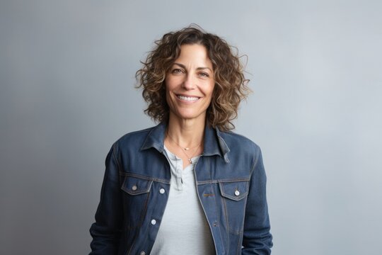 portrait of a Israeli woman in her 50s wearing a denim jacket against a minimalist or empty room background