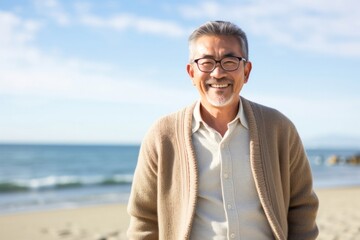 portrait of a Japanese man in his 50s wearing a chic cardigan against a beach background