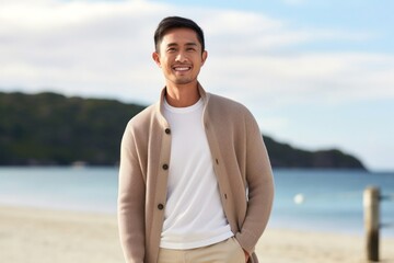 medium shot portrait of a confident Filipino man in his 30s wearing a chic cardigan against a beach background