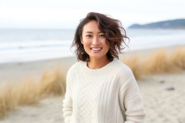 portrait of a Japanese woman in her 30s wearing a cozy sweater against a beach background - obrazy, fototapety, plakaty