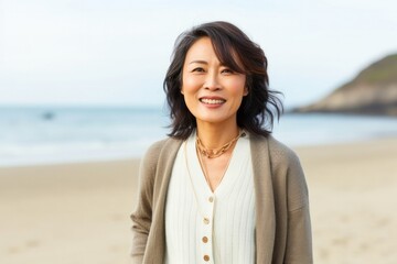 portrait of a Japanese woman in her 40s wearing a chic cardigan against a beach background