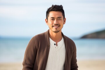 medium shot portrait of a confident Japanese man in his 30s wearing a chic cardigan against a beach background