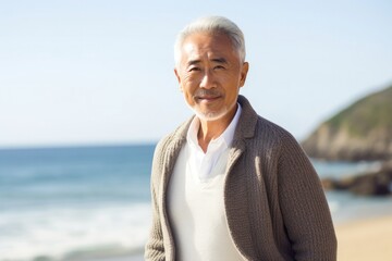 medium shot portrait of a confident Japanese man in his 60s wearing a chic cardigan against a beach background