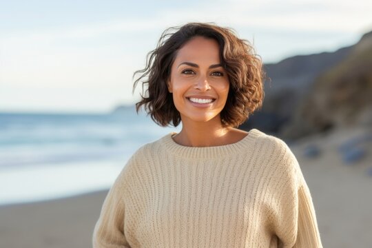 portrait of a Mexican woman in her 40s wearing a cozy sweater against a beach background