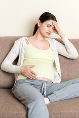 Young pregnant woman with headache sitting on sofa. Pregnancy expectation concept