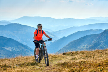 nice senior woman on her electric mountain bike cycling on Feldberg summit with stunning view over the Black Forest mountains and valleys, Baden-Wuerttemberg Germany