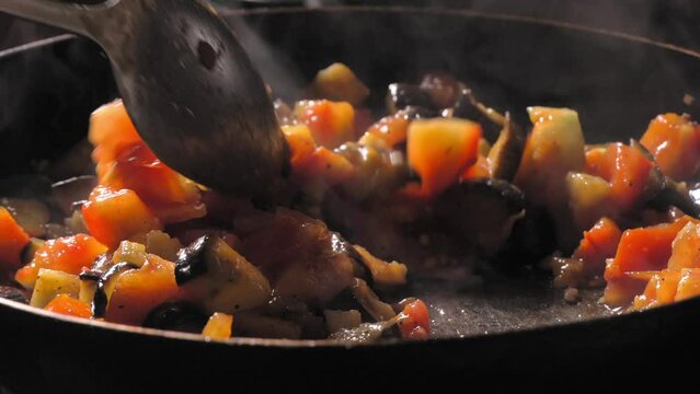 Cooking roasted vegetables. Chef stirs with spoon into steaming hot pan. Asian or vegetarian cuisine. Chef prepares vegetable stew in pan. Increase. Retarded motion.