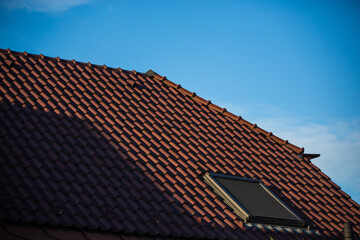 Dark red tile roof with a sunshade equipped window against the blue sky