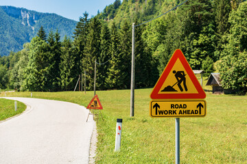 Triangular orange, red and black road work ahead sign or work in progress sign, by the side of a...