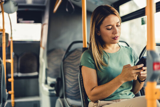 Confident young happy businesswoman commuting to work by bus and having a phone call with her smartphone.