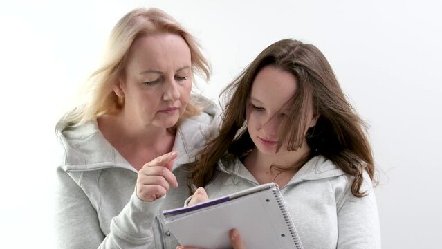 mother and daughter solve math problems together doing homework Girl writes in notebook with pen woman shows finger hint mutual understanding help good relationships in family. adolescence