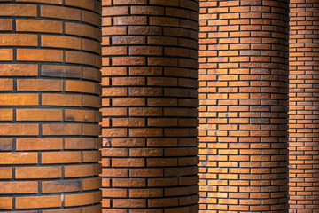 Four columns lined up in a row and faced with red clinker brick. Brick walls of brown brick. Brick wall as background.
