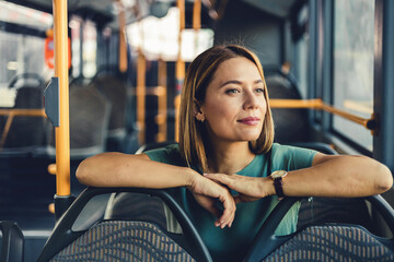 Beautiful woman sitting on the public bus. Woman traveler contemplating outdoor view from window of bus. Young lady on commute travel to work sitting in bus or train. © Jelena Stanojkovic