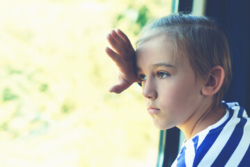 Unhappy sad child looking out the train window. Little boy is traveling on the train. Kid travels on a train.