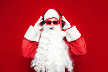 santa claus in hat and glasses listens to music in headphones and sings on red background