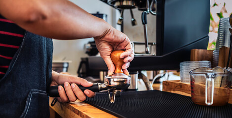 Hand of Barista cafe making coffee with manual presses ground coffee using a tamper making an...