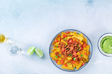 Nachos, Mexican food, tortilla chips with beef and fresh vegetables, overhead shot with tequila, limes, and guacamole sauce, with a place for text