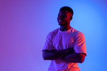 african american man with crossed arms smiling in neon lighting, portrait of young guy in red blue...