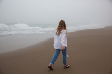 young redhead woman walking on the Oregon Pacific Ocean coast in misty weather