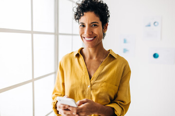 Business woman looking at the camera and using a mobile phone in an office