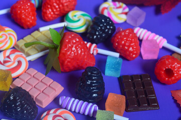 Flat lay of sweet snacks, candies, chocolate,lollipops on purple background