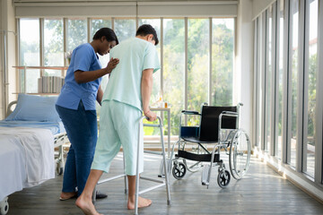 Young female nurse helping young male patient to walk on walker at patient room of hospital