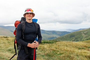 male tourist with backpack and hiking equipment stands in the mountains against the backdrop of...