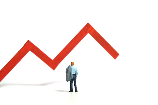 Miniature tiny people toy figure photography. Investment failure and loss concept. A businessman standing in front of red bar declining graph. Isolated on a white background