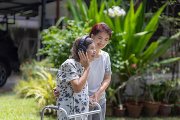 Asian senior woman listening music by headphone with daughterr in backyard.