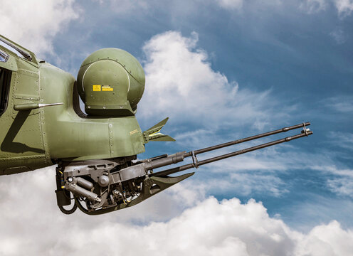 Close-up detail of the military combat helicopter equipped with FLIR camera system and  turret gun in front of blue cloudy sky.