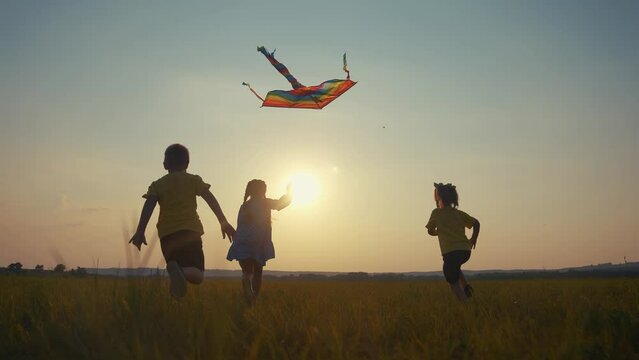 children run with a kite in the park. happy family kid dream concept. a group of children run in the park in nature at sunset playing with a kite. kids silhouette play together in park with kite sun