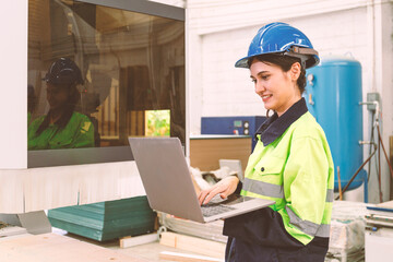 Portrait of a female employee wearing a uniform using a laptop computer. Smiley works in the wood furniture industry.