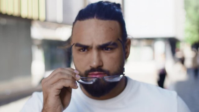 Portrait of a young man putting on glasses close up in the middle of a city street and feeling relief. Young man are starting to use glasses to see more clearly