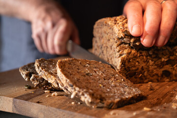 Cutting fresh whole wheat bread into slices on a wooden work surface. Close-up.