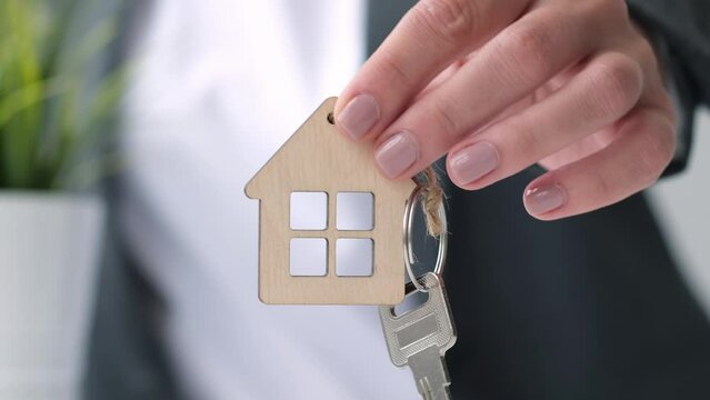Close up female hand of real estate agent or property realtor giving a house key to buyer after singing contract. Mortgage, investment, rent, real estate, property concept. Selective focus
