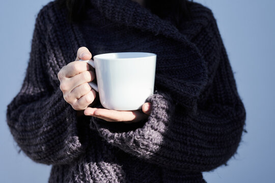 In der K&auml;lte des Winters: Warm eingepackt in einem kuscheligen Pulli, H&auml;nde umschlie&szlig;en eine wei&szlig;e Tasse mit dampfendem Tee. W&auml;rme und Geborgenheit pur