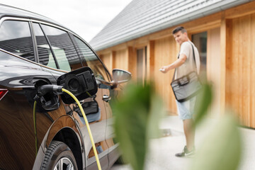 Man plugging a charger in electric car, entering the home door, and remotely locking the vehicle...