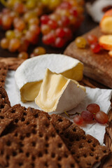Sliced Camembert cheese with grapes and crackers are laid out on a table on a wooden board. the background became. close-up, vertical orientation.