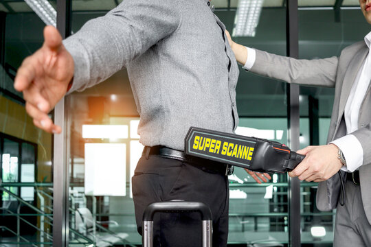 Security man holding metal weapon detector scanner for checking male passenger who going through procedure of physical inspection at entrance airplane gate. Airport security check before flight.