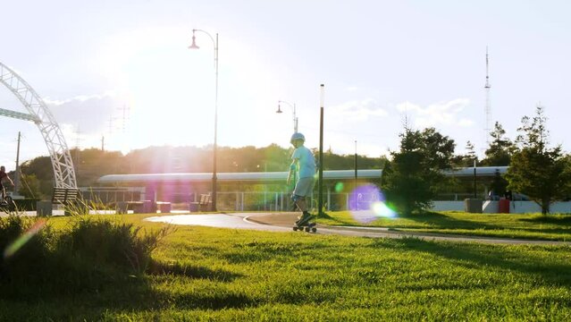 Boy child in protective helmet, active sports equipment. A child riding a skateboard in a city park passing sideways on the path. skateboard lifestyle