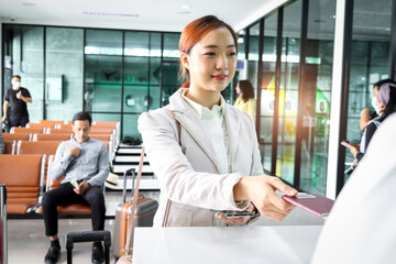 Beautiful Asian female traveler gives passport boarding pass to passenger service agent for checking information at check in area airport terminal, travel on holiday or business trip transportation.