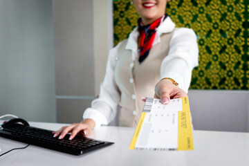 Happy smiling Asian female passenger service agent giving boarding pass ticket to traveler, checking information at check in area airport terminal, traveling or business trip transportation. - obrazy, fototapety, plakaty