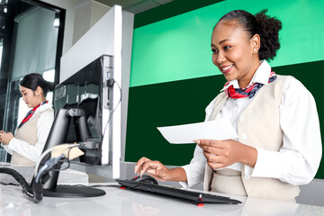 Happy Africa female passenger service agent with curly hair holding boarding pass ticket, checking information on computer at check in area airport terminal, traveling trip airplane transportation. © Stella