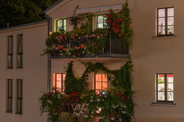 Fototapeta na wymiar old house at night with light in the windows, balconies decorated with flowers and plants.