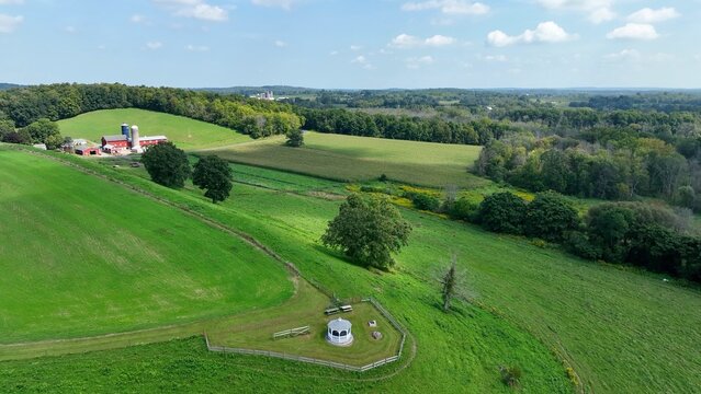 Landscape in New York State countryside with green rolling hills, pastures and farm house under blue sky and white clouds