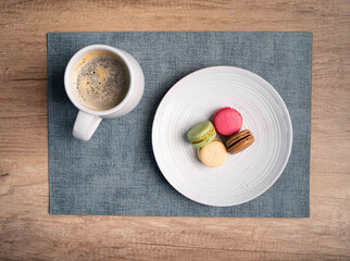 plate of multicolored french macaroons and a cup of coffee on a blue place mat on wooden table at...