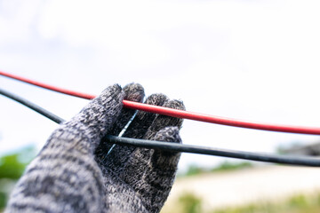 Close-up of a man's hand in a gray woolen glove holding an electric cable.