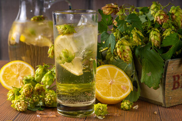 Herbal hop cones and flowers lemonade. Organic raw alternative cold drink, with fresh hop cones, lemon and ice on wooden table copy space